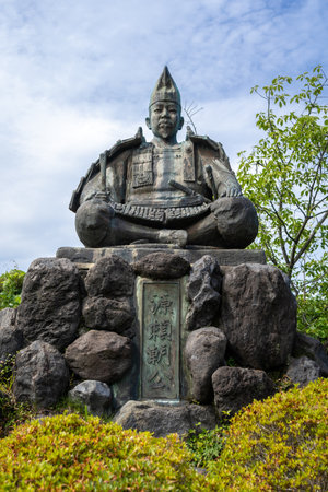 Bronze statue of shogun Minamoto no Yoritomo seated in armor on a stone base in Genjiyama Park, Kamakura, surrounded by greenery and skyの写真素材