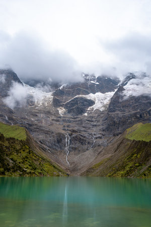 Laguna Humantay, a breathtaking turquoise glacial lake, sits beneath towering Andean peaks partially...
