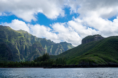 Towering green cliffs dominate Hakaui Bay, Nuku Hiva, Marquesas Islands, French Polynesia. Lush vegetation, palm trees, and deep valleys create a breathtaking natural landscape along the remote Pacific coastlineの写真素材