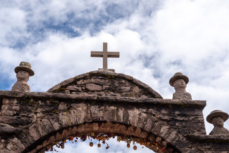 A stone arch with a cross and carved figures marks an entrance in a traditional village on Taquile Island, Lake Titicaca, Peru. The structure is decorated with dried flowers and local ornamentsの写真素材