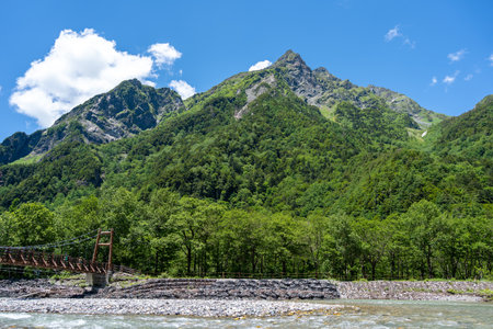 Myojin Bridge stretches over the river beneath towering green peaks on the scenic Kamikochi hiking...