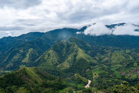 Lush green mountains stretch across the Toraja region in Sulawesi, Indonesia, under a cloudy sky...