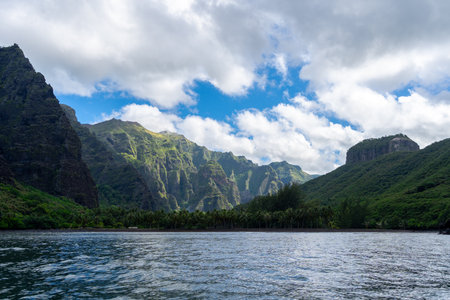 Towering green cliffs dominate Hakaui Bay, Nuku Hiva, Marquesas Islands, French Polynesia. Lush vegetation, palm trees, and deep valleys create a breathtaking natural landscape along the remote Pacific coastlineの写真素材