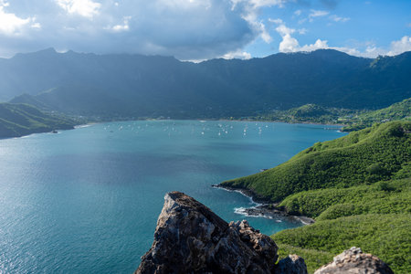 Taiohae Bay in Nuku Hiva, Marquesas Islands, is surrounded by green mountains under a blue and cloudy sky, with sailboats anchored in its calm waters near the coastal town. French Polynesiaの写真素材