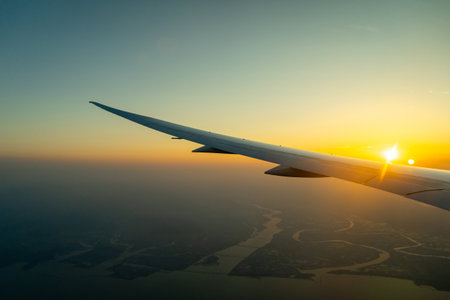 Airplane wing illuminated by the setting sun while descending over the coastline, moments before landing at an airportの写真素材
