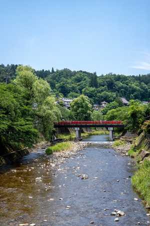 The iconic red Nakabashi Bridge crosses the clear waters of Miyagawa River, surrounded by lush greenery in scenic Takayama, Japanの写真素材