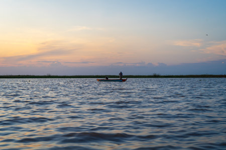 A small boat glides across Lake Tempe at sunset, with golden skies reflecting on the peaceful waters of Sulawesi, Indonesiaの写真素材