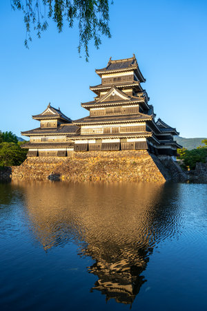 Matsumoto Castle stands majestically as golden light reflects off its dark wooden exterior and calm surrounding waters in Matsumoto, Japanの写真素材