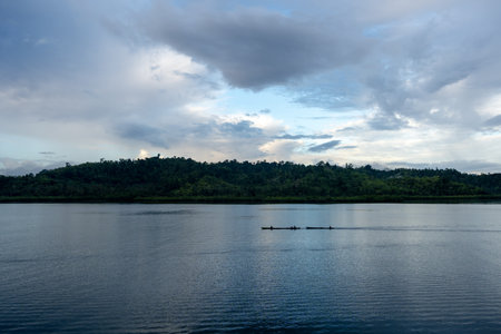 A traditional canoe glides over the calm sea at sunset, surrounded by the serene beauty of the...