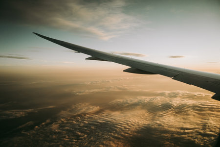 Airplane wing captured at golden hour with soft yellow light illuminating the clouds below, creating a peaceful and dreamlike atmosphere at high altitudeの写真素材