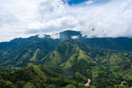 Lush green mountains stretch across the Toraja region in Sulawesi, Indonesia, under a cloudy sky with mist clinging to the ridgelinesの写真素材