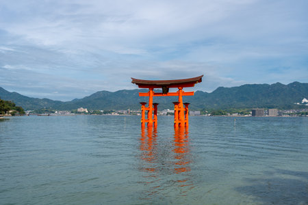 The famous floating torii gate of Itsukushima-jinja shrine stands in the sea near Miyajima Island, with calm waters and green hills surrounding it. Near Hiroshima, Japanの写真素材