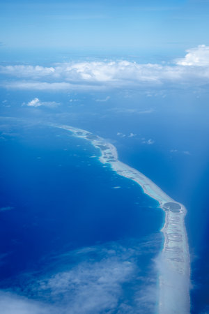 The Tuamotus atoll in French Polynesia emerges from the deep blue Pacific Ocean, partially covered by scattered clouds. The turquoise lagoon contrasts beautifully with the darker surrounding watersの写真素材