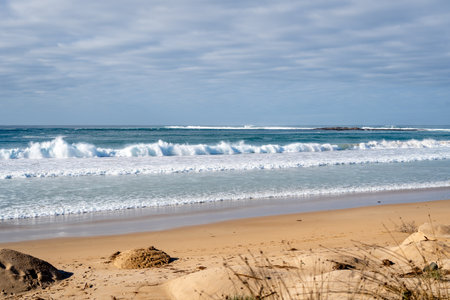 A vast sandy beach stretches along the Great Ocean Road, Australia, with gentle waves lapping the...