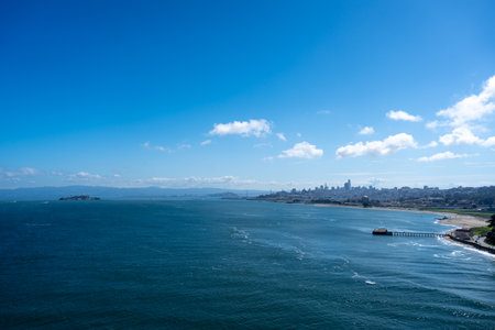 The skyline of San Francisco stretches across the horizon, with the deep blue waters of the bay and a pier along the shorelineの写真素材