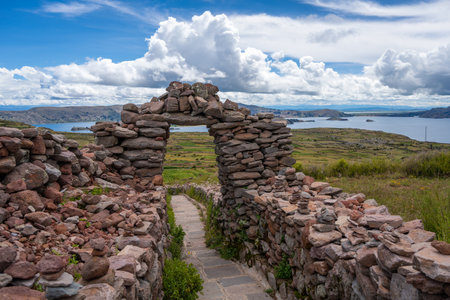 A stone arch marks the entrance to a paved path at the Pachatata archaeological site on Amantani Island, Peru, overlooking Lake Titicaca and terraced fieldsの写真素材