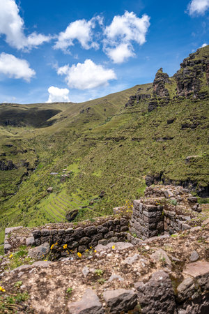 Ancient stone walls and terraces of Waqrapukara blend into the surrounding green mountains, highlighting Inca engineering in this remote Andean landscape under a bright skyの写真素材