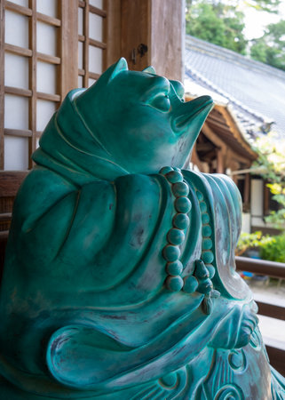 A playful turquoise Tanuki statue wearing prayer beads stands peacefully at Daisho-in Temple on the forested Miyajima Island in southern Japanの写真素材