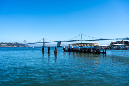 A peaceful view of the waterfront in San Francisco, featuring the Oakland Bay Bridge, calm blue...