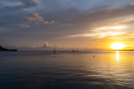 A beautiful sunset over Tahaa Island in French Polynesia, with calm waters and sailboats creating a...