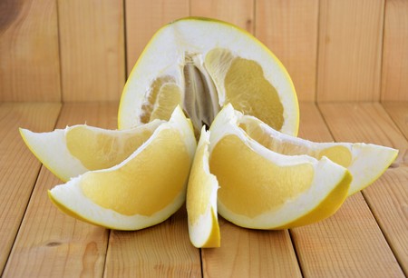 A half of yellow fresh pomelo and it's pieces on simple wooden background, close up of fruitの写真素材