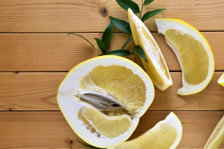 A half of yellow fresh pomelo and it's pieces on simple wooden background with green decorative leafs, close up of fruitの写真素材