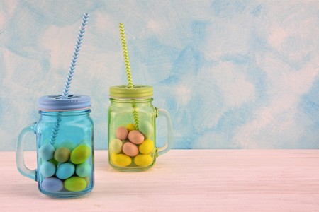 Sky-blue and green transparent glass jars with colored Easter eggsの写真素材