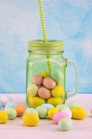 Green transparent glass jar with colored Easter eggs and green straw