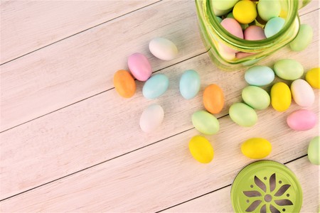 Green transparent glass jar with colored Easter eggs on the white wooden background