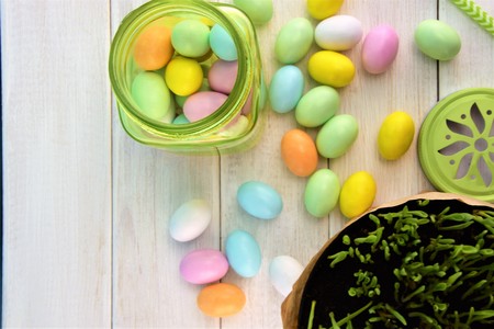Green transparent glass jar with colored Easter eggs on the white wooden table background, decorative view from aboveの写真素材