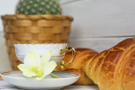 Vintage coffee cup with espresso on a saucer, croissants, cactus in basket, green orchid flower on a white wooden backgroundの写真素材