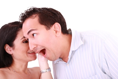 girl tells something into surprised guy's ear isolated on white backgroundの写真素材