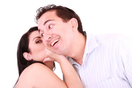 pretty girl talking secret to young man in his ear, man smiling over isolated white background の写真素材