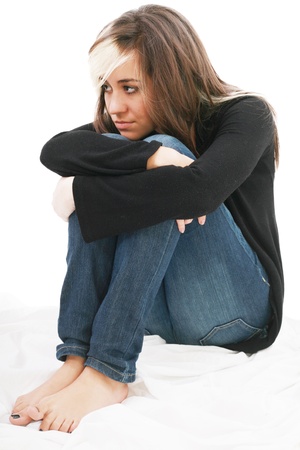 Sad girl teenager sits twining arms about legs. Isolated on a white background. の写真素材