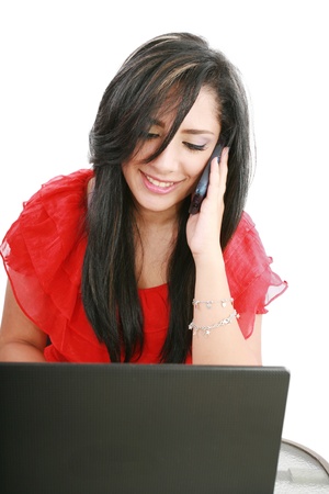 Portrait of a smiling young business woman speaking on mobile phone while using laptop in office 
の写真素材