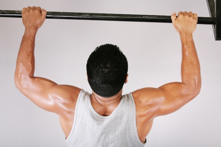 Reaching Goal: Strong man doing pull-ups on a bar in a gymの写真素材