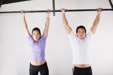 Female and male bodybuilder doing pull-ups on metal bar on gymの写真素材