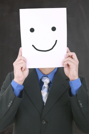 Young businessman hiding his face with a white billboard with a smiley face on it 
の写真素材