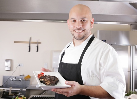 young male chef presenting a juicy ribeye steak with tomatoesの写真素材