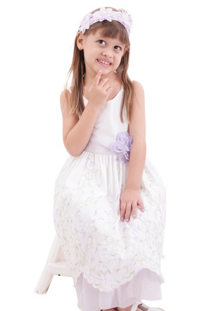 little girl wearing white dress and posing on chair on white background の写真素材