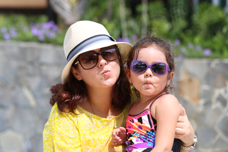 Portrait of mother and daughter giving a kiss to the camera. Focus in the little girlの写真素材