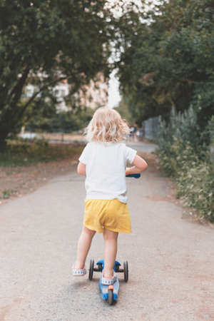 Outdoor portrait of a happy white young girl riding a scooter.の写真素材