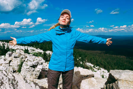 A happy tourist-traveler standing in mountains with his hands raised.