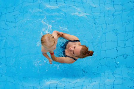 Happy family. Mom teaches her daughter 2-3 years old to swim in the pool. Top view.の写真素材
