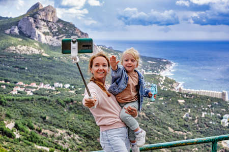 Mother and daughter making a selfie on background of excellent mountains, clouds and the sea. The concept of family travelの写真素材