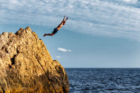 A man jumps into the sea from a high cliffの写真素材