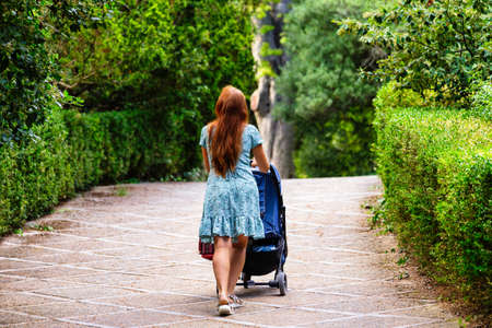 Back view of mother walking with her baby in stroller in parkの写真素材