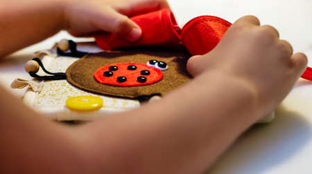 A child plays with an educational toy red ladybug made of felt. Montessori concept, early education.の写真素材