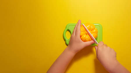 A child cuts a toy pepper on a yellow background with a toy knifeの写真素材