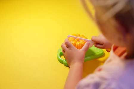 A child cuts a toy pepper on a yellow background with a toy knifeの写真素材